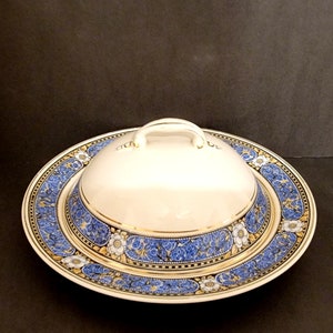 May include: A white ceramic butter dish with a blue and gold floral design. The lid has a gold handle.