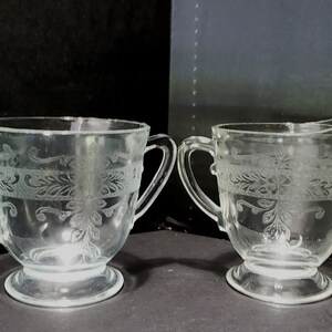 May include: A set of two clear glass sugar and creamer containers with an etched floral design.