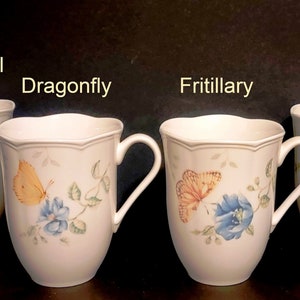 Könnte beinhalten: Vier weiße Keramikbecher mit Schmetterlingsmotiven. Die Becher sind mit "Swallowtail", "Dragonfly", "Fritillary" und "Monarch" beschriftet.