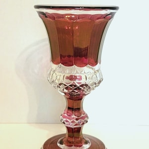 Peut inclure: Un gobelet en verre rouge rubis vintage avec un motif en verre taillé. Le gobelet a un bol large et évasé et une tige haute et fine.
