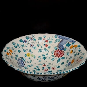 May include: A white ceramic bowl with a scalloped edge and a floral design in shades of blue, green, yellow, red, and orange.