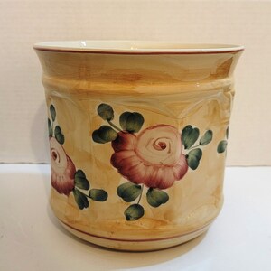May include: A yellow ceramic planter with a floral design. The planter features pink and white roses with green leaves. The planter has a slightly rounded shape.