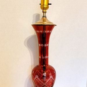 May include: A red glass table lamp with a white etched design. The lamp has a brass base and a gold-colored socket.