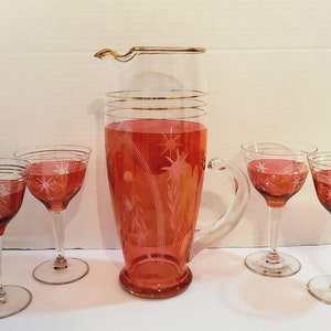 May include: A set of five vintage glass cocktail glasses with a pink and white starburst design. The set includes a pitcher and four glasses.