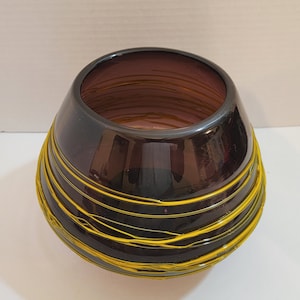 May include: A dark purple glass bowl with yellow swirling lines. The bowl is round and has a wide opening.