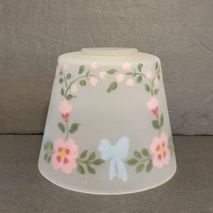 May include: A frosted glass lampshade with a floral design. The shade features pink and white flowers, green leaves, and a blue bow.