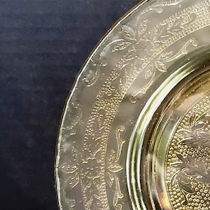 May include: A vintage yellow glass plate with a gold embossed floral design. The plate has a scalloped edge and a raised rim.