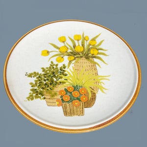 May include: A white ceramic plate with a brown rim features a floral design of yellow tulips and orange flowers in woven baskets. The plate has a speckled background.