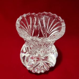 Può includere: Un vaso da fiori in vetro trasparente con un design in cristallo tagliato. Il vaso ha un'ampia apertura e una base rotonda.