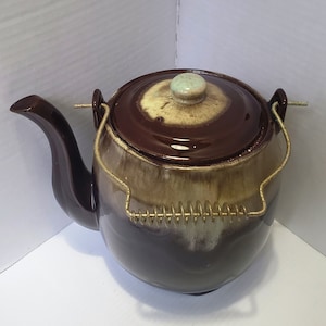 May include: A brown and beige ceramic teapot with a lid and a metal handle. The teapot has a brown glaze with a beige swirl pattern.