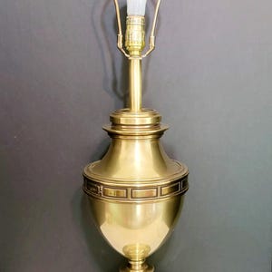 May include: A brass table lamp with a classic design. The lamp features a bulb, a tall, fluted base, and a decorative band around the middle. The lamp is approximately 30 inches tall.