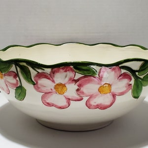 Könnte beinhalten: Eine weiße Keramikschüssel mit einem gewellten Rand und einem Blumendesign. Die Schüssel ist mit rosa und weißen Blumen mit grünen Blättern verziert.