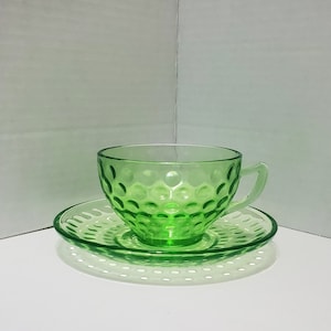 Può includere: Un set da tè in vetro verde con una tazza e un piattino con un design testurizzato e a puntini.