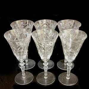 May include: Set of six clear glass wine glasses with etched floral designs. The glasses have a tall, slender stem and a round bowl.