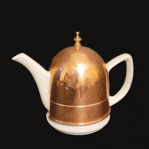 May include: A white teapot with a copper lid and a brass knob. The teapot has a white base and a copper band around the lid.