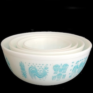 Könnte beinhalten: Ein Satz von vier weißen Rührschüsseln mit türkisfarbenem Design. Die Schüsseln sind ineinander verschachtelt. Das türkisfarbene Design umfasst einen Hahn, Pflanzen und Menschen. Die Schüsseln bestehen aus einem dicken, undurchsichtigen Material.