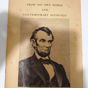 May include: A black and white illustration of Abraham Lincoln on the cover of a book titled "Abraham Lincoln: From His Own Words and Contemporary Accounts". The book cover is yellowed with age and has a quote from Lincoln: "I Would Save the Union."