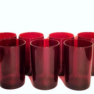 Può includere: Set di otto bicchieri rossi rubino. Questi bicchieri alti e cilindrici hanno un design semplice ed elegante. I bicchieri sono realizzati in vetro rosso scuro e sono disposti su una superficie bianca. Perfetti per servire acqua, succo o cocktail.
