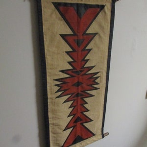 May include: A beige fabric wall hanging with a geometric pattern of red and black triangles. The hanging is attached to a wooden dowel rod.