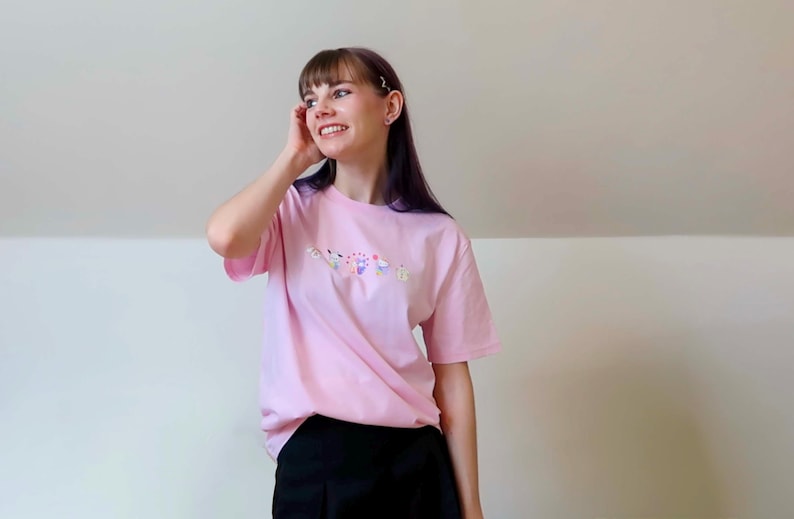 May include: A light pink t-shirt with a floral design. The shirt is short-sleeved and has a crew neck. The model is wearing black shorts.