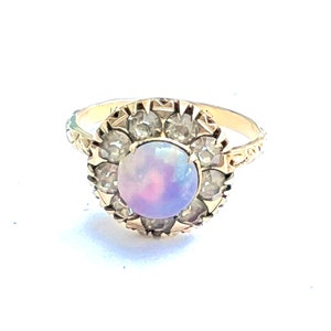 May include: A gold ring with a large, round, iridescent opal surrounded by smaller, clear stones.