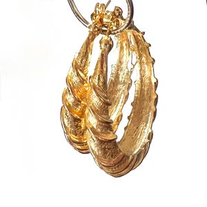 May include: A pair of gold-toned hoop earrings featuring a textured, spiraled surface design. The earrings are suspended from a circular metal ring, showcasing a metallic finish with ridges that create a distinct, repeating pattern along the hoops.