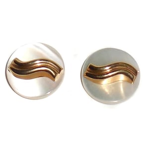 May include: A pair of round stud earrings. Each earring features a gold-colored, wave-like design on a pearlescent, circular base. The earrings are set against a white background.