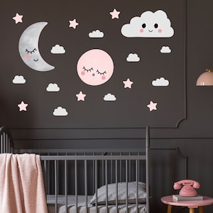 May include: A nursery wall decal set with a pink and gray color scheme. The set includes a crescent moon, a sun, a cloud, and stars. The moon, sun, and cloud have cute faces.