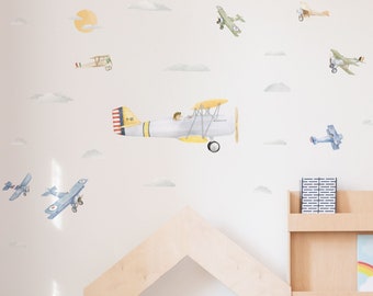 May include: A set of 9 airplane wall decals in various colors and styles, including a yellow and white biplane with a pilot, a blue biplane, and a green biplane. The decals are perfect for a nursery or child's room.