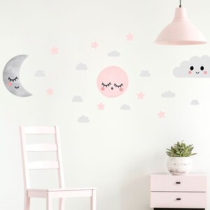 May include: A pink and gray nursery wall decal set featuring a sleeping moon, a sleeping sun, a smiling cloud, and stars. The decals are on a white wall with a pink chair and a pink nightstand.