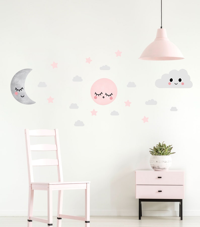 May include: A pink and gray nursery wall decal set featuring a sleeping moon, a sleeping sun, a smiling cloud, and stars. The decals are on a white wall with a pink chair and a pink nightstand.