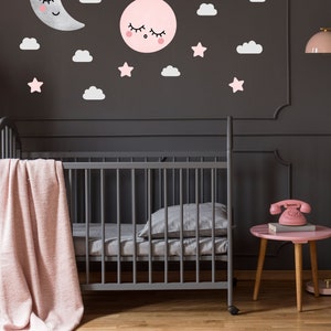 May include: A gray crib with a pink blanket and a gray pillow. The wall behind the crib is dark gray and has pink and white clouds, stars, and a moon and sun with faces on them.