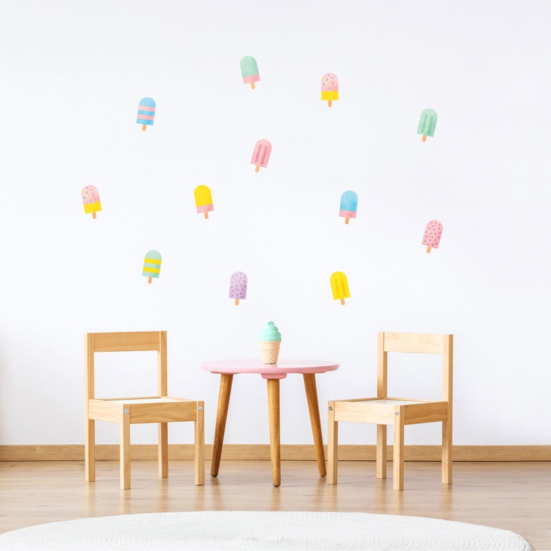 May include: A pink table and two wooden chairs with a white rug underneath. The wall behind the table is decorated with colorful popsicle stickers.