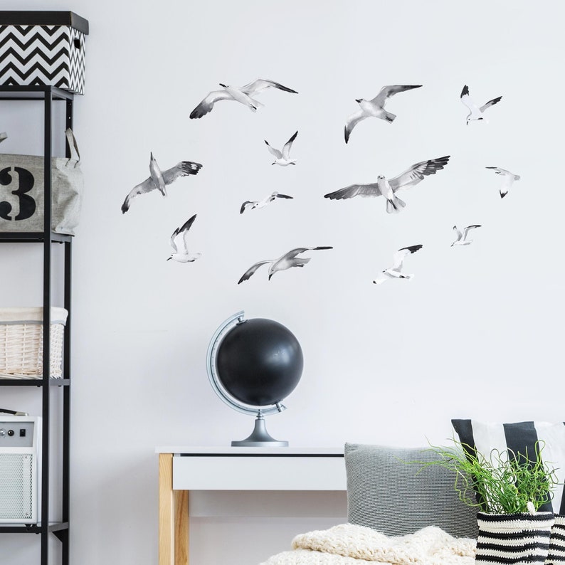 Puede incluir: Una pared blanca con un globo terr&aacute;queo negro y una colecci&oacute;n de calcoman&iacute;as de gaviotas blancas y negras. Las calcoman&iacute;as est&aacute;n dispuestas en un patr&oacute;n disperso, creando una sensaci&oacute;n de movimiento y vuelo.