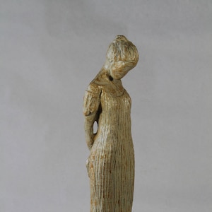 May include: A ceramic sculpture of a person in a long dress, with a textured surface and a light brown and white color scheme.