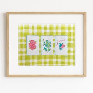Puede incluir: Una impresi&oacute;n enmarcada con tres naipes ilustradas sobre un fondo de cuadros verdes y amarillos. Las cartas muestran una flor rosa, un dise&ntilde;o de pavo real y un p&aacute;jaro con la palabra "joker". La obra tiene un estilo caprichoso.