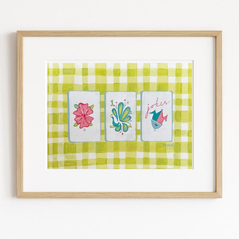 Puede incluir: Una impresi&oacute;n enmarcada con tres naipes ilustradas sobre un fondo de cuadros verdes y amarillos. Las cartas muestran una flor rosa, un dise&ntilde;o de pavo real y un p&aacute;jaro con la palabra "joker". La obra tiene un estilo caprichoso.