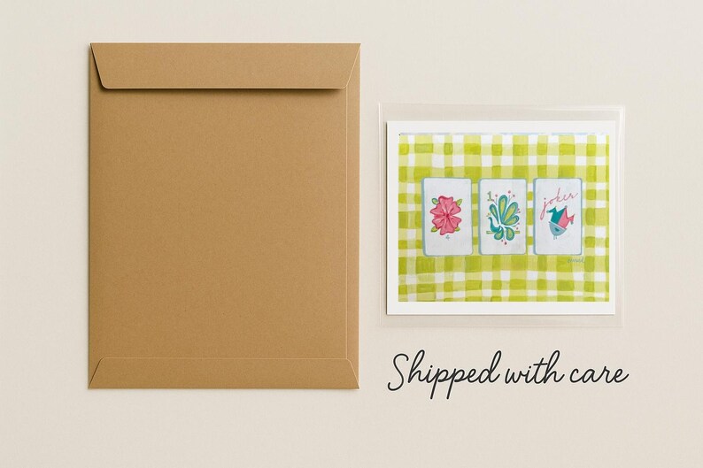 Puede incluir: Un sobre de papel marr&oacute;n junto a una impresi&oacute;n enmarcada de tres naipes. Las cartas presentan ilustraciones de acuarela de flores y un p&aacute;jaro sobre un fondo a cuadros verde y blanco. La palabra "Joker" est&aacute; en una carta.