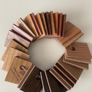 May include: A circular fan-shaped collection of rectangular wood veneer samples in various shades of brown, ranging from light tan to dark espresso. The samples are held together by a metal ring, and one piece features the text Dms Design tea modern furniture.