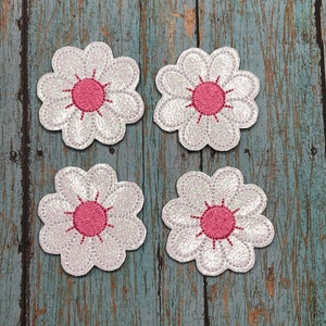 May include: Four white felt flower patches with pink centers. The flowers have a glittery finish.