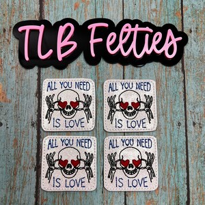 May include: Four white felt patches with embroidered skulls with red hearts for eyes and the text "All you need is love" in blue lettering.