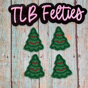 May include: Four green felt Christmas tree ornaments with red stitching and red wavy lines. The ornaments are on a wood background with the text "TLB Felties" in pink letters on a black background.