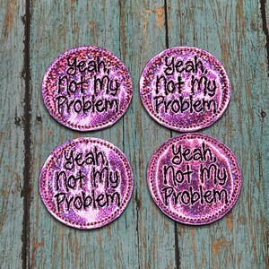 May include: Four pink and iridescent round iron-on patches with the text "Yeah, Not My Problem" in black.