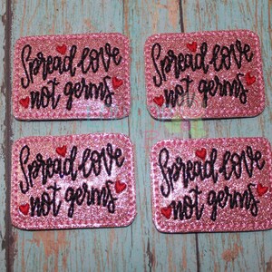 May include: Four pink glitter iron-on patches with the text "Spread love not germs" in black cursive font and red hearts.