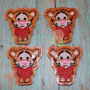 May include: Four orange and brown glitter iron-on patches of Tigger from Winnie the Pooh holding a red heart.