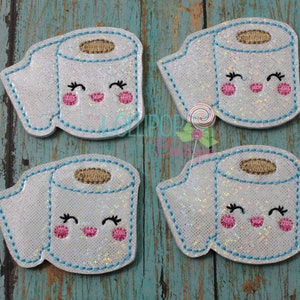 Puede incluir: Cuatro parches de rollo de papel higiénico blanco brillante con caras sonrientes, pestañas y mejillas rosadas. Cada parche tiene un contorno cosido en azul claro y un centro marrón. Los parches están dispuestos sobre una superficie de madera turquesa y marrón.