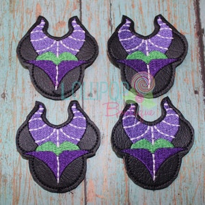May include: Four purple and green embroidered patches of a character with horns and a webbed design. The patches are on a wooden background.