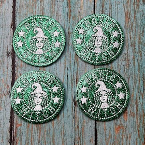 May include: Four green and white glitter coasters with a witch and the text "Brew Witch" in a circle.