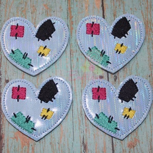 May include: Four blue felt heart-shaped patches with colorful embroidered details, including red, yellow, green, and black patches. The patches have a stitched appearance, resembling a patchwork heart.