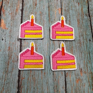 May include: Four pink and yellow embroidered cake slice patches with a single orange candle on top. The patches are on a light blue wooden background.